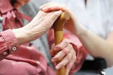 A close-up of a senior's hands on walking stick, with a younger person's hands on top of their hands.