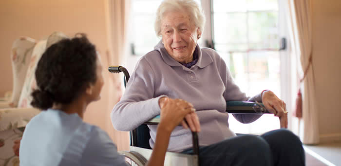 A woman in a wheelchair visits with an aide.