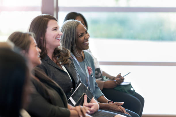 A group of diverse women sitting on the front row enjoy the comments made by the speaker at the conference.