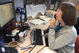 A woman in an office answering a call while working on a computer